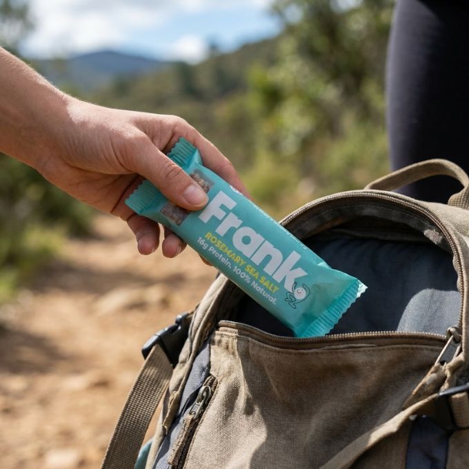 A person taking a Frank Protein Bar out of their bag mid hike