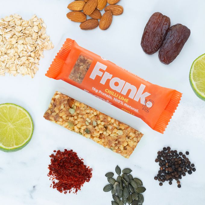 Frank Protein Bar both packaged and unpackaged surrounded ingredients in the bar such as oats and dates.