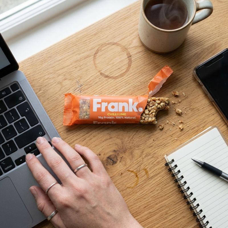 A open Frank protein bar a an office desk with a bit taken out of it and crumbs falling out.