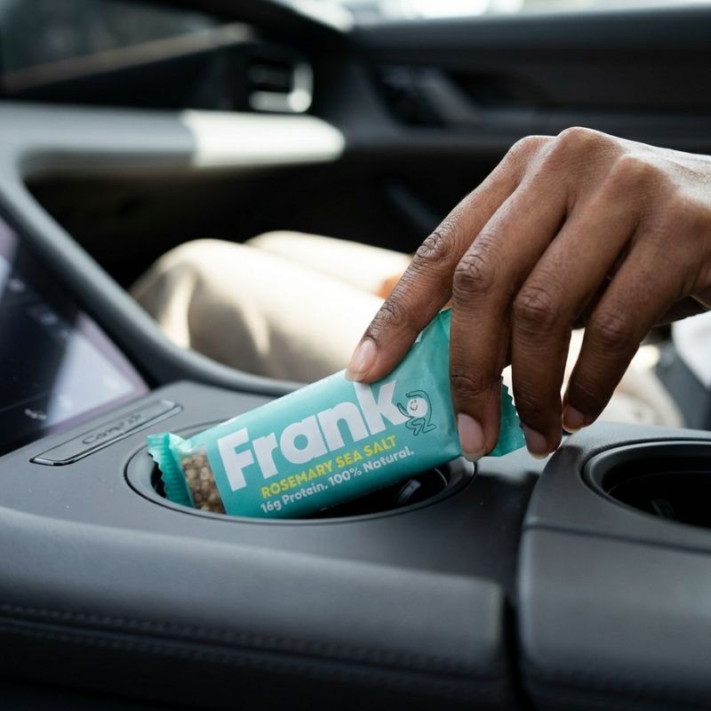 Person reaching for Frank Protein bar in cup holder in a car